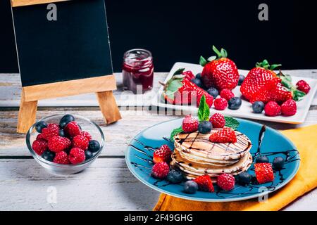 Weißen Teller voll mit Pfannkuchen mit Erdbeeren Himbeeren Heidelbeeren und Honig auf weiß Stockfoto