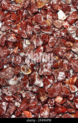 Schöne Textur aus rotem nassem Granit in Form von feinem Kies in polierten Stücken, abgerundet und poliert. Vertikale Farbfotografie, Nahaufnahme. Stockfoto