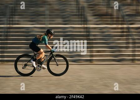 Seitenansicht der professionellen Radfahrerin in Radbekleidung und Schutzausrüstung Fahrrad fahren in der Stadt, hetzen und vorbei an Gebäuden während des Trainings Stockfoto