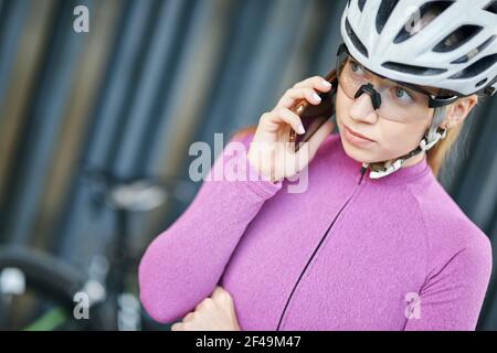 Porträt einer fokussierten jungen sportlichen Frau, Radfahrerin mit Schutzkleidung, die mit dem Smartphone einen Anruf macht, während sie mit ihrem Fahrrad im Freien steht Stockfoto