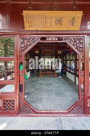 Suzhou, China - 3. Mai 2010: Bescheidener Verwaltungsgarten. Geschnitzte hölzerne kastanienfarbene Eingangstür zum offenen Raum mit großem Brett oben mit Manda Stockfoto