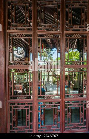 Suzhou, China - 3. Mai 2010: Bescheidener Verwaltungsgarten. Blick durch kunstvoll geschnitzte Fenster von außen durch den Flur hinter in das Grün Stockfoto