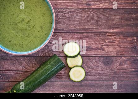 Frische Gemüsesuppe aus Erbsen auf einem Teller auf braunem Holztisch mit Gurken und grünem Pfeffer, Draufsicht mit Platz für Text. Lecker Stockfoto