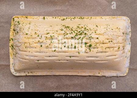 Gefrorenes Blätterteig mit Lachs auf Backpapier liegend, isoliert auf einem braunen Hintergrund Draufsicht. Stockfoto