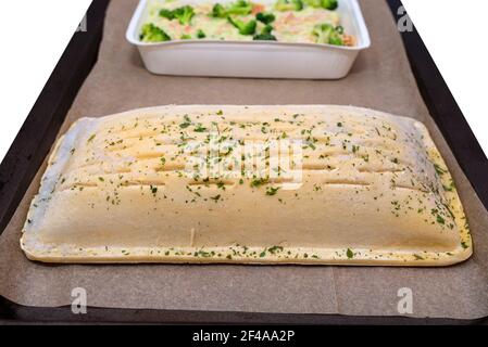 Gefrorener Blätterteig mit Lachs und pollock-Filet mit Brokkoli und gerösteten Mandeln in einer Sahnesauce auf Backpapier liegend, isoliert auf einem weißen Backgr Stockfoto