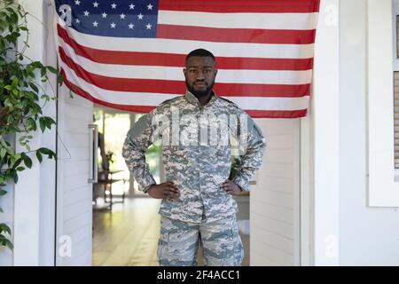 afroamerikanischer Soldat, der vor der amerikanischen Flagge steht Außerhalb des Hauses Stockfoto