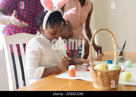 Glückliche afroamerikanische Eltern mit Sohn und Tochter im Hase Ohren malen bunte Eier Stockfoto