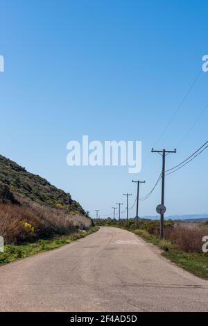 Die Zufahrtsstraße führt durch Hügel, die mit Strommasten unter blauem Himmel gesäumt sind. Stockfoto