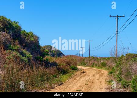 Rauer Feldweg kurvt Hügel mit Telefonmasten unter Blau Himmel Stockfoto