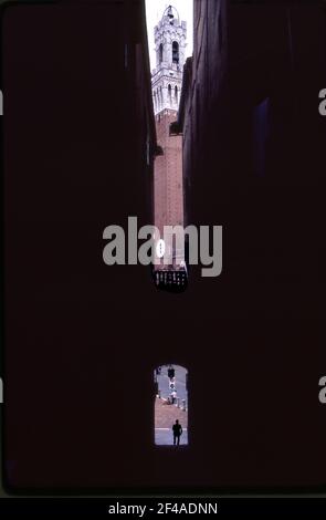 Glockenturm in Siena, Italien gesehen durch Gebäude auf einer schmalen Straße, die zum Campo führt. Stockfoto