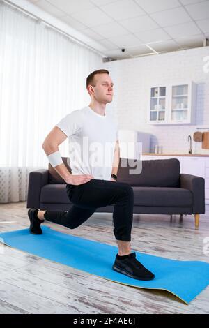 Muskulöser, athletischer Mann in einem T-Shirt, der zu Hause Aufwärmübungen macht. Sport zu Hause während der Quarantänezeit. Fitness außerhalb des Fitnessraums Stockfoto