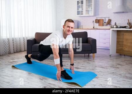 Muskulöser, athletischer Mann in einem T-Shirt, der zu Hause Aufwärmübungen macht. Sport zu Hause während der Quarantänezeit. Fitness außerhalb des Fitnessraums Stockfoto