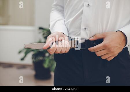 Die Hände eines Mannes in einem weißen Hemd und Schwarze Hose zum Befestigen des Gürtels Stockfoto