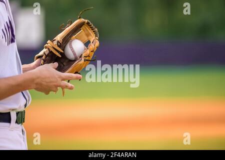 Ein junger erwachsener männlicher Baseballspieler, der einen Baseballhandschuh und einen Baseballball in seinem Handschuh hält. Stockfoto