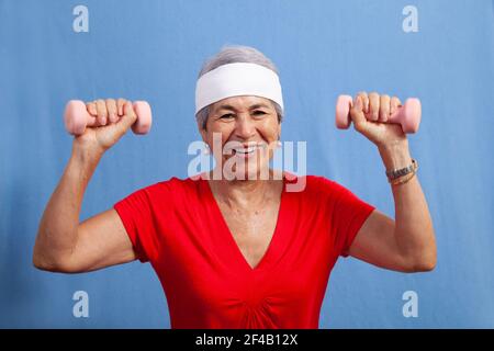 Attraktive ältere grauhaarige hispanische Frau in einem Schweißband Gewichtheben, lächelnd und glücklich. Stockfoto