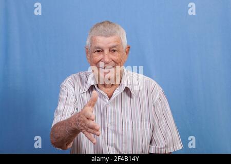Aktiver glücklicher älterer Mann mit grauem Haar und einer sonnengeschädigten Haut, die sich ausstreckt, um die Hände beim Gruß zu schütteln, während sie lächelt. Stockfoto
