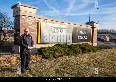 Ein Polizeibeamter posiert auf dem Schild, das den Hauptcampus der Purdue University Fort Wayne bezeichnet. Stockfoto