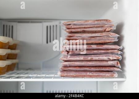 Viele tiefgekühlte Fleischverpackungen in einem Stapel im Gefrierschrank mit Vakuum versiegelt. Gemahlenes Huhn und pute inklusive Rücken, Nacken, Leber und Herz. Rohkost Ernährung fo Stockfoto