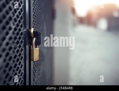 Vorhängeschloss an der Außentür, Nahaufnahme. Im Gewerbe- oder Wohngebiet im Käfig. Goldenes Metallschloss auf schwarzem Zaun mit verstärktem Netz. Sicherheitshintergrund tex Stockfoto