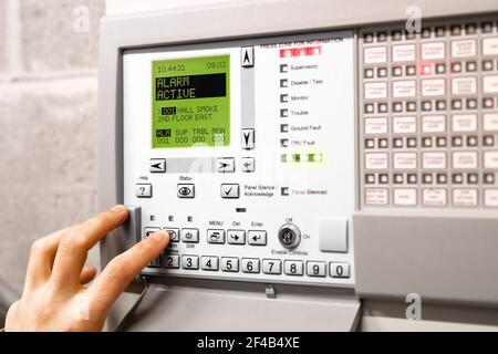 Die Brandmeldezentrale ist aktiviert und befindet sich im Alarmmodus. Display-Meldung: Alarm aktiv Hall Smoke. Rote flackernde Lichter und Piepen. Eine Hand verwendet Stockfoto