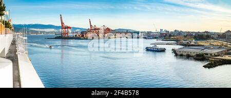 Vancouver Hafenpanorama am frühen Morgen, an einem sonnigen Tag. Skyline der Stadt am Wasser mit Industrie. Eine Seabusfähre verlässt die Hafenstation. Stockfoto