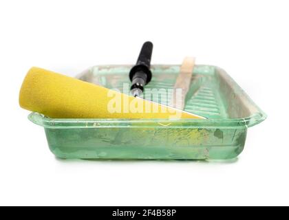 Gebrauchte und gereinigte Farbwalze und -Pfanne. Vorderansicht der großen gelben groben Schaumwalze in grüner Kunststoffschale mit Schichten von Farbe kleben. Konzept für Heimwerker Stockfoto