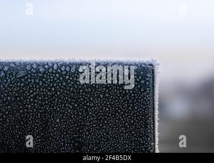 Frost oder Eiskristalle an der Ecke aus schwarzem Metall am frühen Morgen, nahe dem Sonnenaufgang. Schöne dünne Eisschicht auf fester Oberfläche mit Glatteisglättungstemperatur Stockfoto