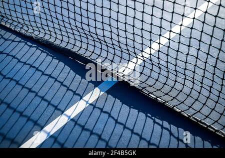 Abstraktes Tennis Court Sport Textur. Unfokussieren perspektivische Ansicht der weißen Mitte Service-Linie durch das Netz, draußen frühmorgens. Blau gummiert und gr Stockfoto