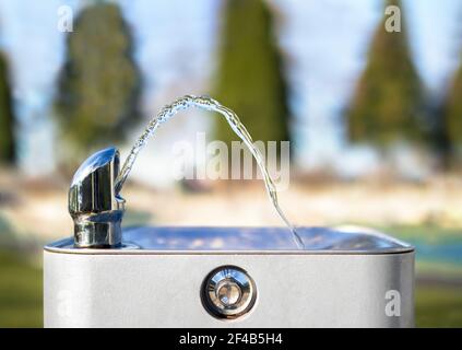 Trinkwasserbrunnen im Park an einem sonnigen Tag, keine Person. Nahaufnahme von fließendem Wasser aus der Lasche in einem Bogen. Heller, unschärfender Park. Stockfoto