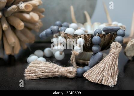 Anordnung von Holz Perlenketten drapiert über Schale auf Tisch. Blaue und weiße Perlen. Gedämpfte braune, grüne und blaue Farben. Dekoration im Hintergrund. Stockfoto