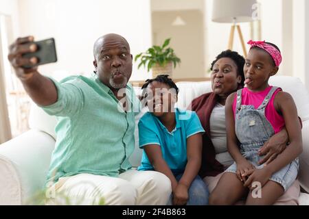 afroamerikanische Großvater und Großmutter auf Couch machen Gesichter mit Enkelkinder nehmen Selfie Stockfoto