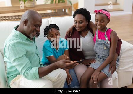 Glücklicher afroamerikanischer Großvater und Großmutter auf der Couch mit Enkeln Smartphone betrachten Stockfoto
