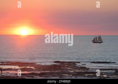 Broome ist eine Küstenstadt, Perlstadt und Touristenstadt in der Kimberley-Region von Western Australia. Foto zeigt Cable Beach bei Sonnenuntergang und ein Segelboot. Stockfoto