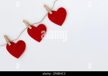 Weißer Hintergrund mit drei roten Herzen auf Wäscheklammern. Valentinskarte. Stockfoto