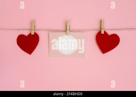 Papierblätter auf Faden mit herzförmiger Wäscheklammer auf rosa Hintergrund. Alles Liebe zum Valentinstag, Muttertag. Stockfoto