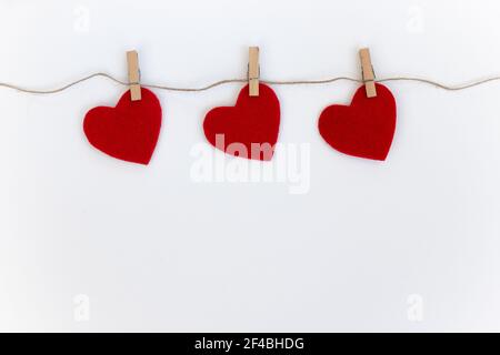 Weißer Hintergrund mit drei roten Herzen auf Wäscheklammern. Valentinskarte. Stockfoto