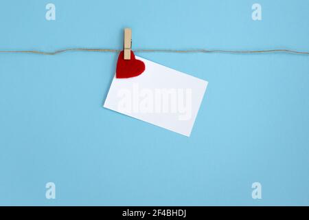 Weißes Stück Papier mit Wäscheklammer am Seil befestigt, auf blauem Hintergrund. Alles gute zum Valentinstag. Stockfoto