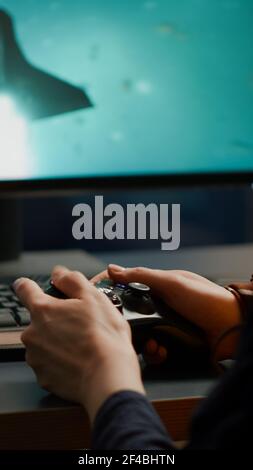 Nahaufnahme der wettbewerbsfähigen Frau Spieler mit Joystick spielen Weltraum-Shooter-Videospiele an leistungsstarken Computer spät in der Nacht. Professioneller Gamer mit Wireless-Controller für Online-Gaming-Meisterschaft Stockfoto
