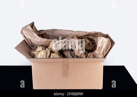 Öffnen Sie den Karton auf einem schwarzen Tisch, mit Papierfüllung. Für sicheren Transport während Paketdienst, Wiederverwendung, Umwelt Stockfoto