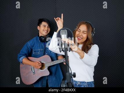 Junge asiatische Frau tanzt, schwingt und hebt ihre Arme rhythmisch beim Singen. Musiker, die Musik im professionellen Aufnahmestudio produzieren. Stockfoto