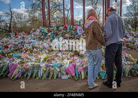 Ein Paar schaut auf florale Tributes links Clapham Common Bandstand, wo die Menschen weiterhin ihre Achtung zu Sarah Everard am 16. März zahlen, 2021 in Lo