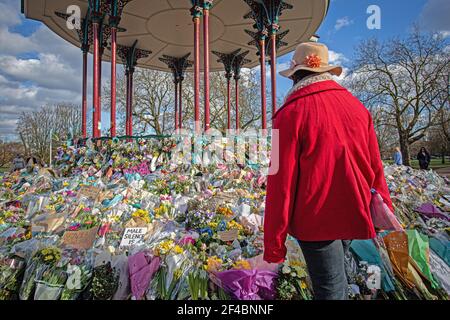 Eine Frau schaut auf florale Tribute links Clapham Common Bandstand, wo die Menschen weiterhin ihren Respekt zu Sarah Everard am 16. März zahlen, 2021