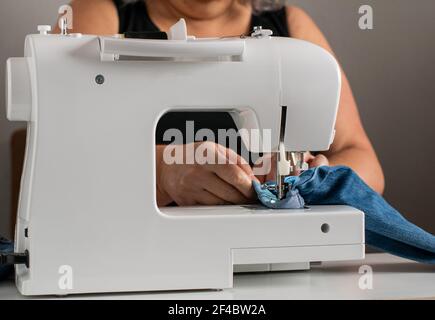 Vorderansicht einer Nähmaschine, mit einer älteren, unkenntlich kaukasischen Frau im Hintergrund, die Näharbeit leistet. Stockfoto