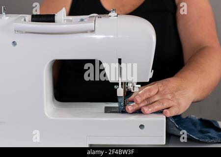 Vorderansicht einer Nähmaschine, mit einer älteren, unkenntlich kaukasischen Frau im Hintergrund, die Näharbeit leistet. Stockfoto