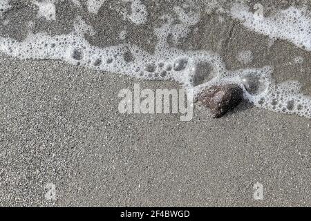 Sanfte Welle am schwarzen vulkanischen Sandstrand. Hintergrund mit Kopierbereich. Stockfoto