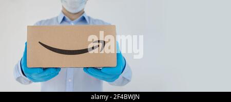 Lieferer hält Kartons Amazon in medizinischen Handschuhen und Schutzmaske auf weißem Hintergrund. Die Versandzeit Coronavirus. Stockfoto