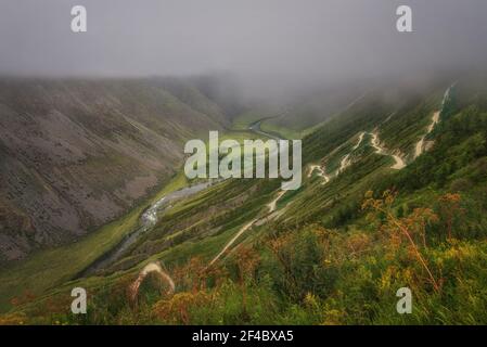 Landschaftlich schöne Aussicht auf steilen Berghang mit gewundenen Feldsteinstraße, Teil des Berges Serpentin durch Pass, Wald und Flusstal gegen backdr Stockfoto