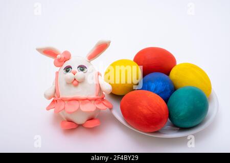 Frohe Ostern Konzept. Handbemalte Ostereier und ein handgemachtes Knethasen in rosa Rock auf weißem Hintergrund, Draufsicht. DIY. Lustige Dekoration. Stockfoto