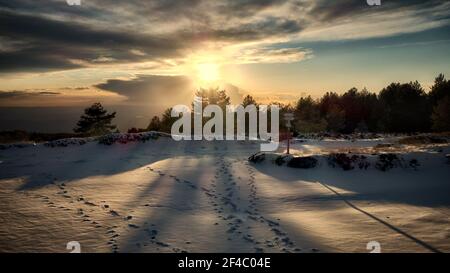 Winteransicht in Sizilien bei Sonnenuntergang geht die Sonne unter Am Horizont auf verschneite Landschaft mit Kiefernwald Und Wolken am Himmel des Naturparks ETN Stockfoto