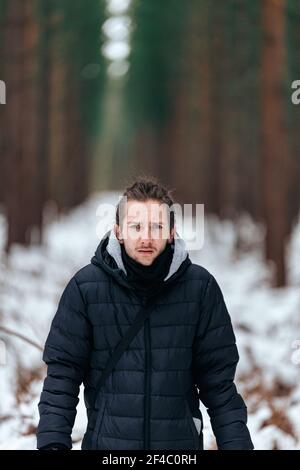 Hübscher junger Mann, der in einem verschneiten Wald steht und gerade aussieht In die Kamera Stockfoto